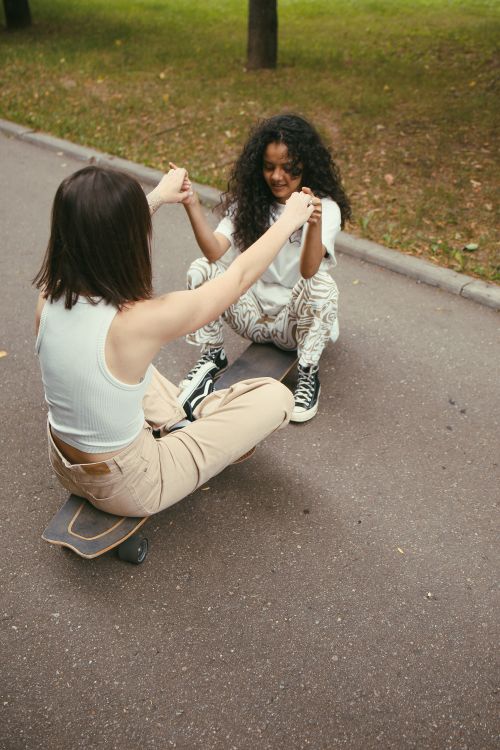 Free Two women having fun with a skateboard, holding hands and smiling outdoors. Stock Photo