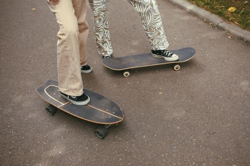 Free Two skateboarders in stylish attire glide smoothly outdoors on the road. Stock Photo