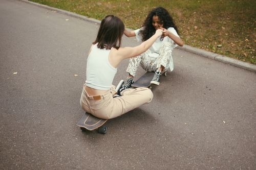 Free Two young women enjoying a playful skateboard ride on a sunny day in the park. Stock Photo