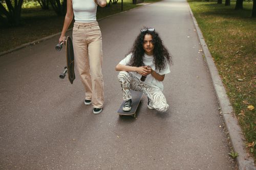Free Two young women enjoy skateboarding on a sunny park road, embracing an active lifestyle. Stock Photo