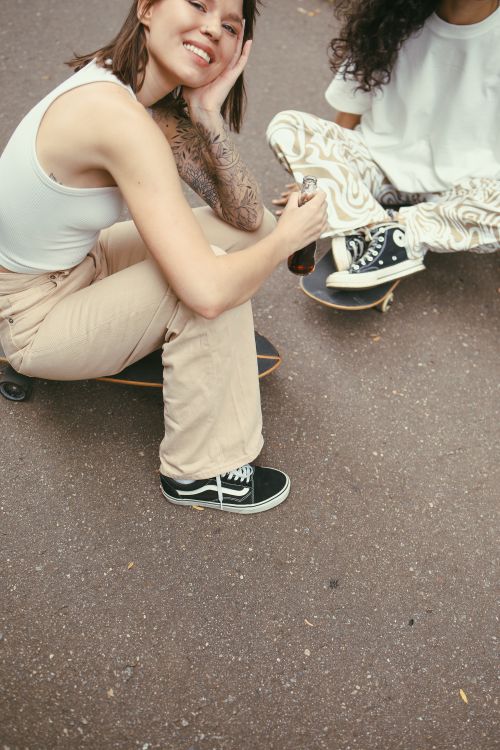 Free Two young women enjoying skateboarding while holding soft drinks outdoors. Stock Photo