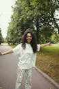 Woman in White Long Sleeve Shirt Standing on Gray Concrete Road