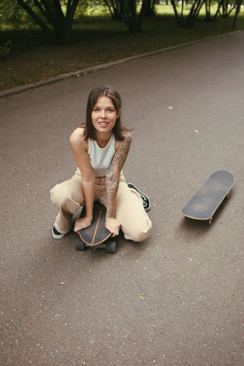 Free Smiling young woman with tattoos sits on skateboard outdoors, embodying street style. Stock Photo