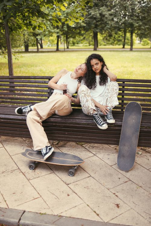 Free Two women sitting on a bench with skateboards in a park, enjoying a relaxed moment. Stock Photo