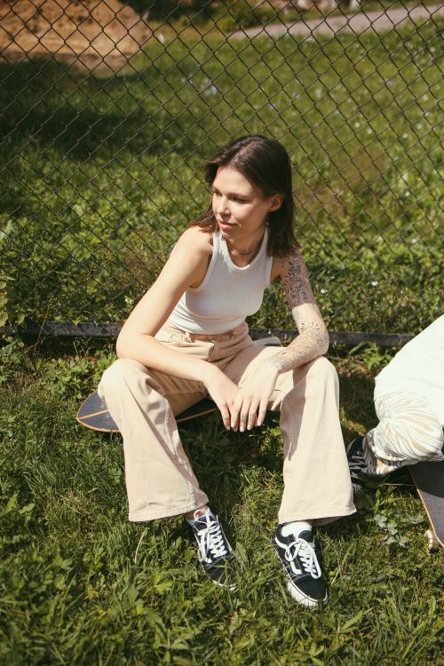 Free Young skater woman with tattoos sitting on grass, relaxed and thoughtful. Stock Photo