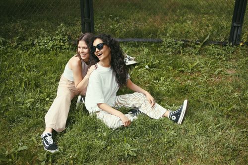 Free Two women sitting on grass, smiling and enjoying a sunny day together outside. Stock Photo