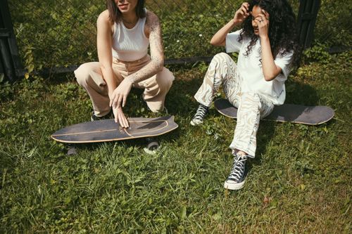Free Two young women skateboarders sitting on grass, enjoying a sunny day. Stock Photo