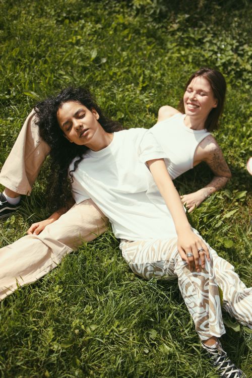 Free Two friends relaxing on grass, enjoying a sunny day outdoors, embodying comfort and friendship. Stock Photo