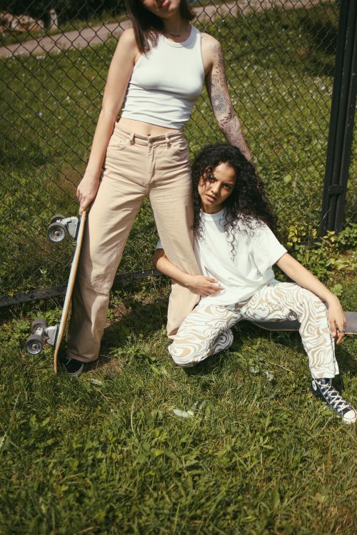 Free Two young women hanging out with a skateboard in a grassy area outdoors. Stock Photo