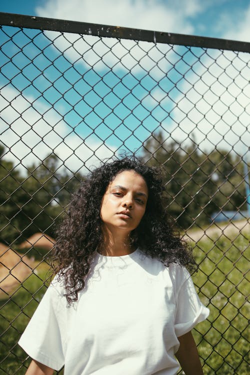 Woman in White T Shirt Posing near Metal Chain Link Fence
