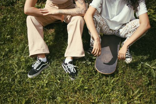 Free Two skaters sitting on grass with a skateboard, enjoying the sunny day together. Stock Photo