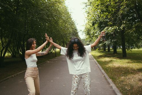 Free Two women happily high-fiving in the park, enjoying a sunny day together. Stock Photo