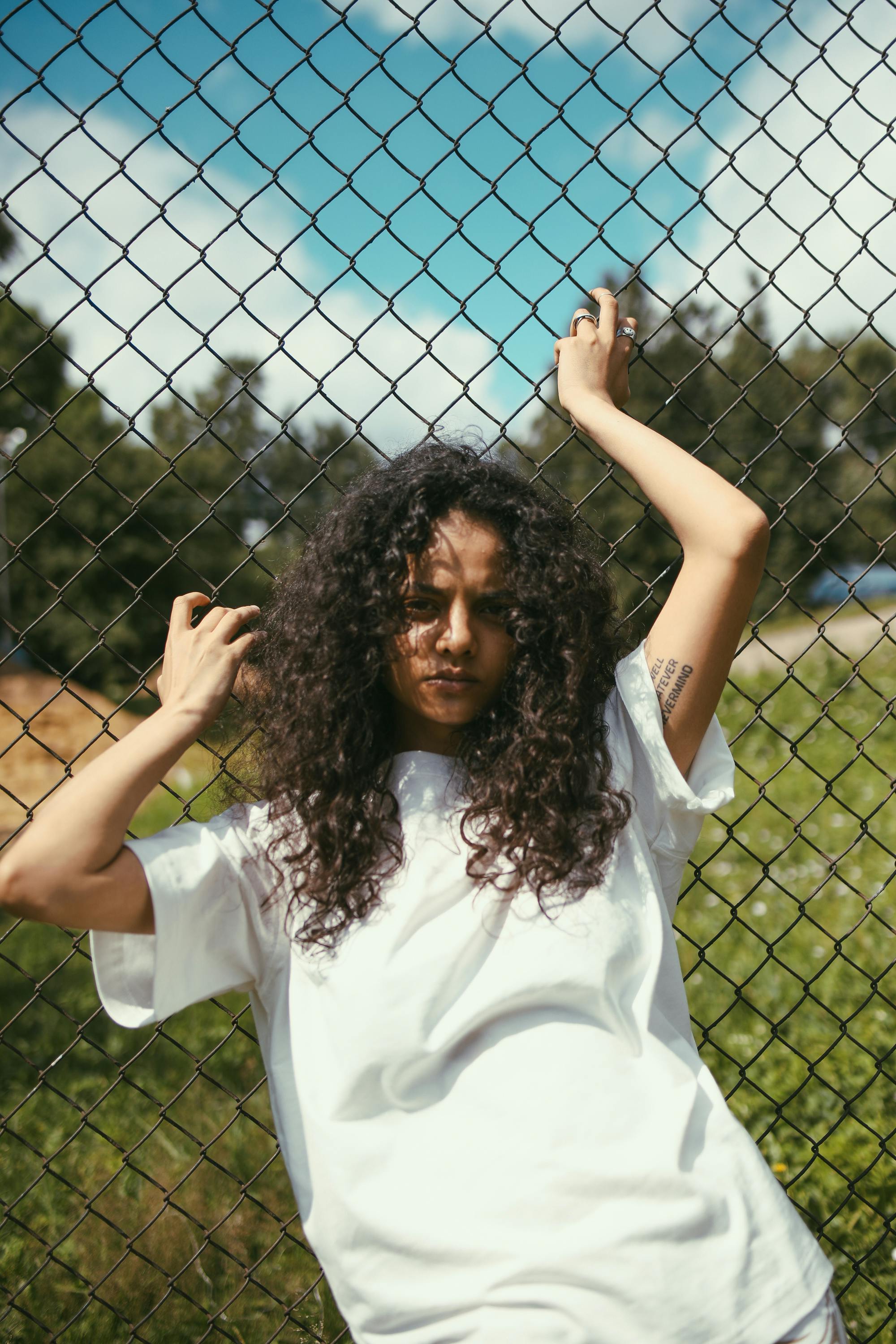 woman in white shirt standing beside chain link fence