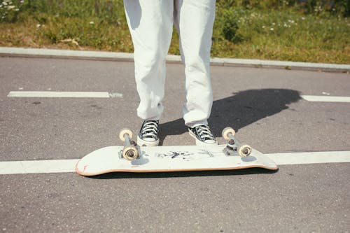Person in White Pants and White and Black Sneakers Riding Skateboard
