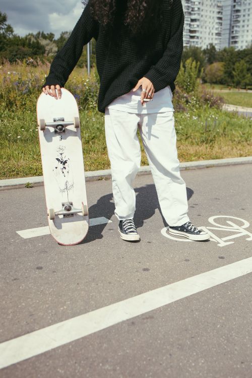 Free A skateboarder casually holding a board on a sunny day, standing on an urban path. Stock Photo