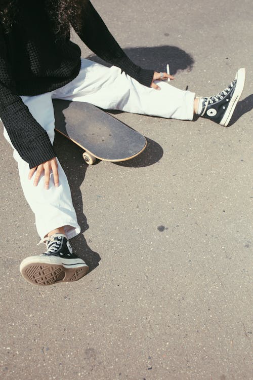 High-Angle Shot of a Person Sitting on Skateboard while Smoking Cigarette