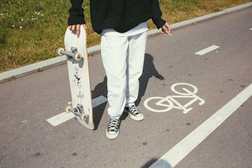 High-Angle Shot of a Person Standing Holding a Skateboard while Smoking Cigarette