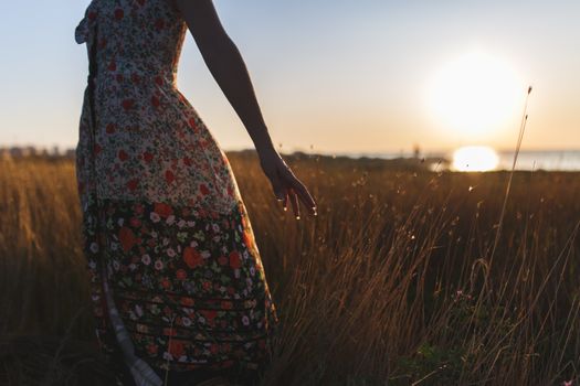 Silhouette of a woman wearing a floral dress standing in a field at sunset.