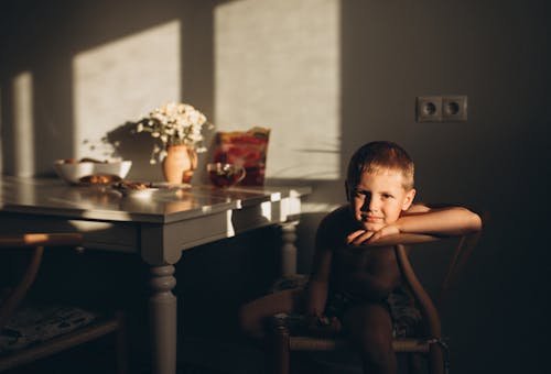 Free Young boy sitting in a dimly lit dining room, creating a cozy and relaxed atmosphere. Stock Photo