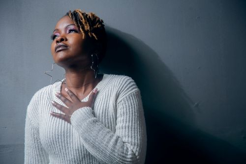 Free Portrait of a black woman with dreadlocks in a white sweater, looking up thoughtfully indoors. Stock Photo