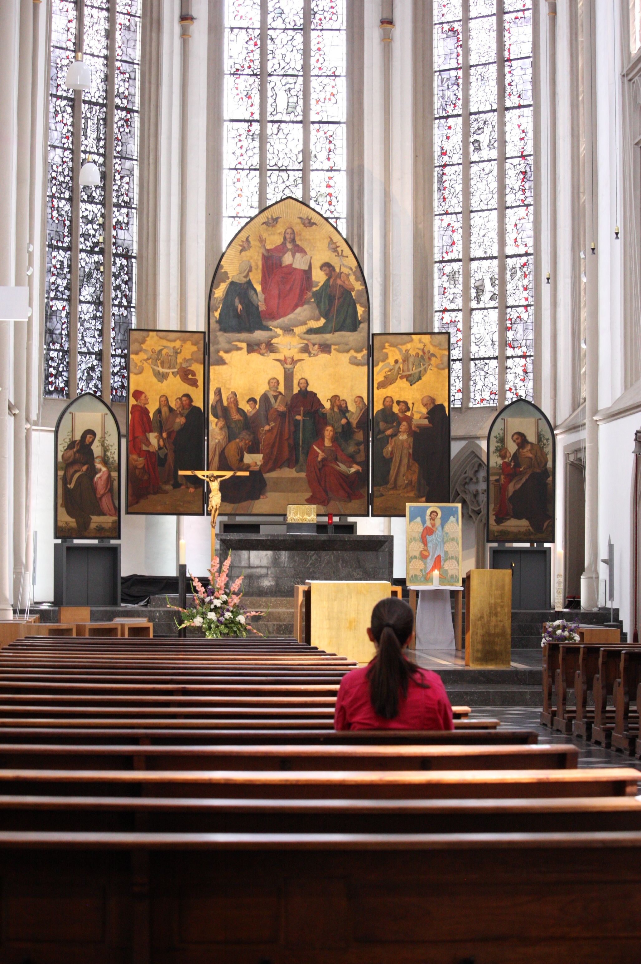 A serene church interior showcasing an altar, stained glass, and religious artwork with a woman in prayer.