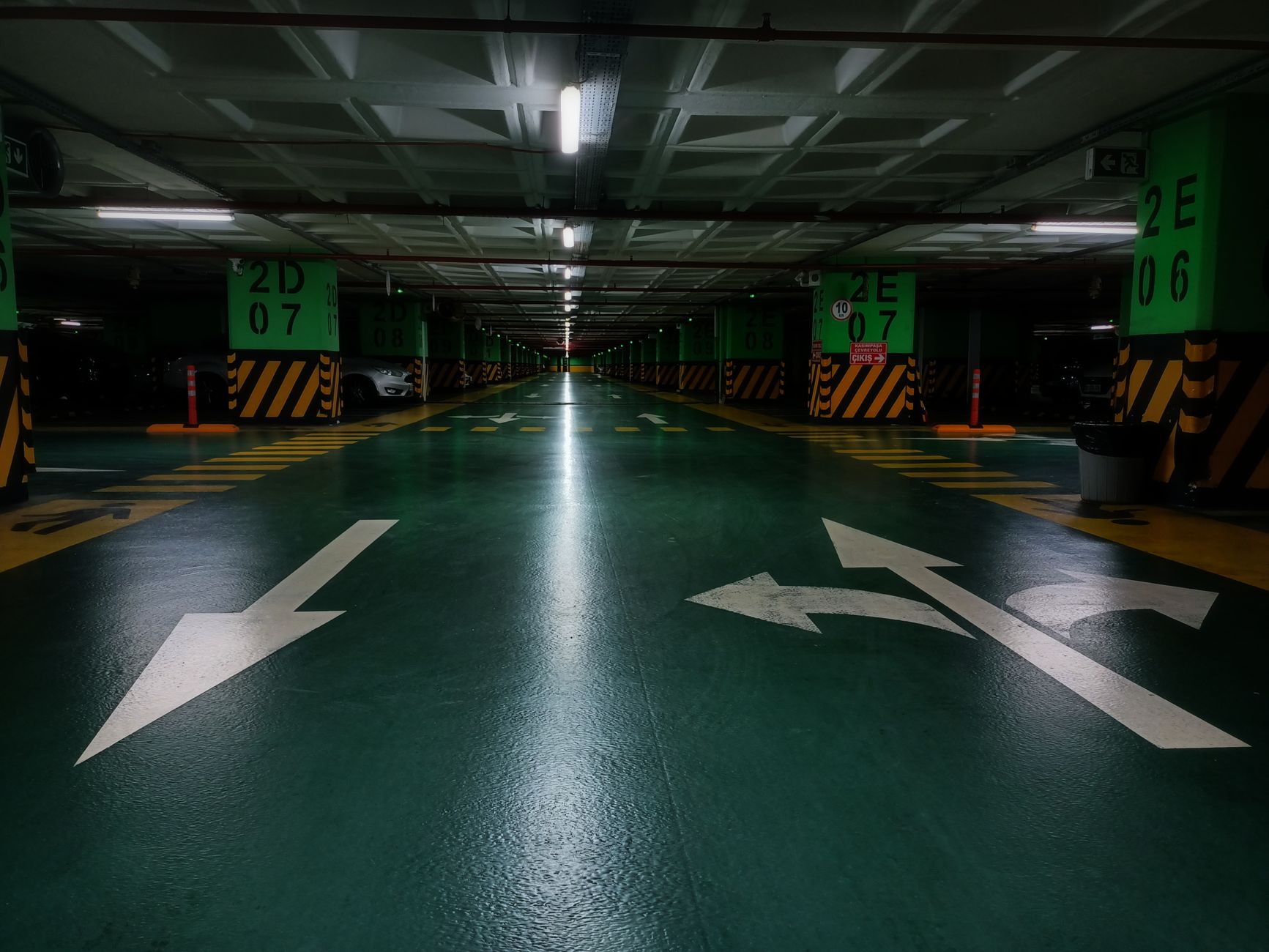 Dimly lit underground parking lot with directional arrows and green floor marking.