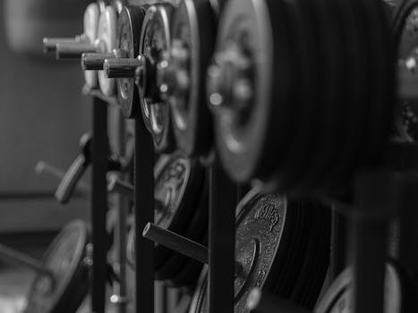 Black and white close-up of steel exercise weights in a gym setting.