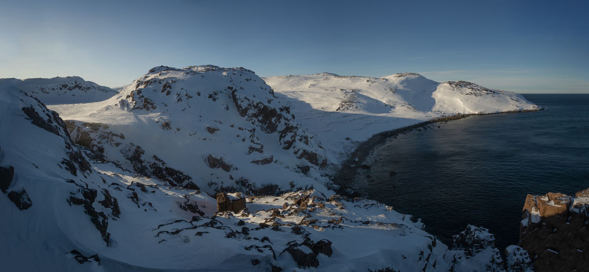 Stunning winter coastal landscape in Teriberka, Russia, featuring snow-covered mountains and a frozen lake.