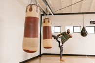 Man in Green Jacket and Gray Pants Sitting on Red and Brown Hanging Heavy Bag