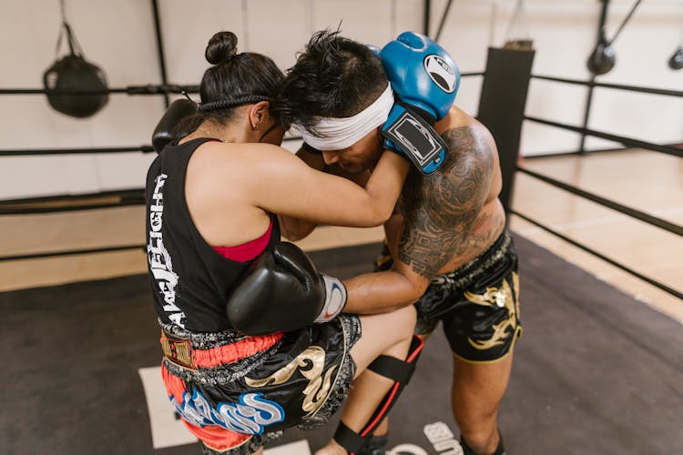 A Woman In Sports Wear With Blue Boxing Gloves Kicking A Man In The Sparring Ring