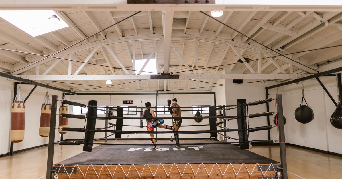 Two athletes engage in an intense sparring session in a well-lit boxing gym.