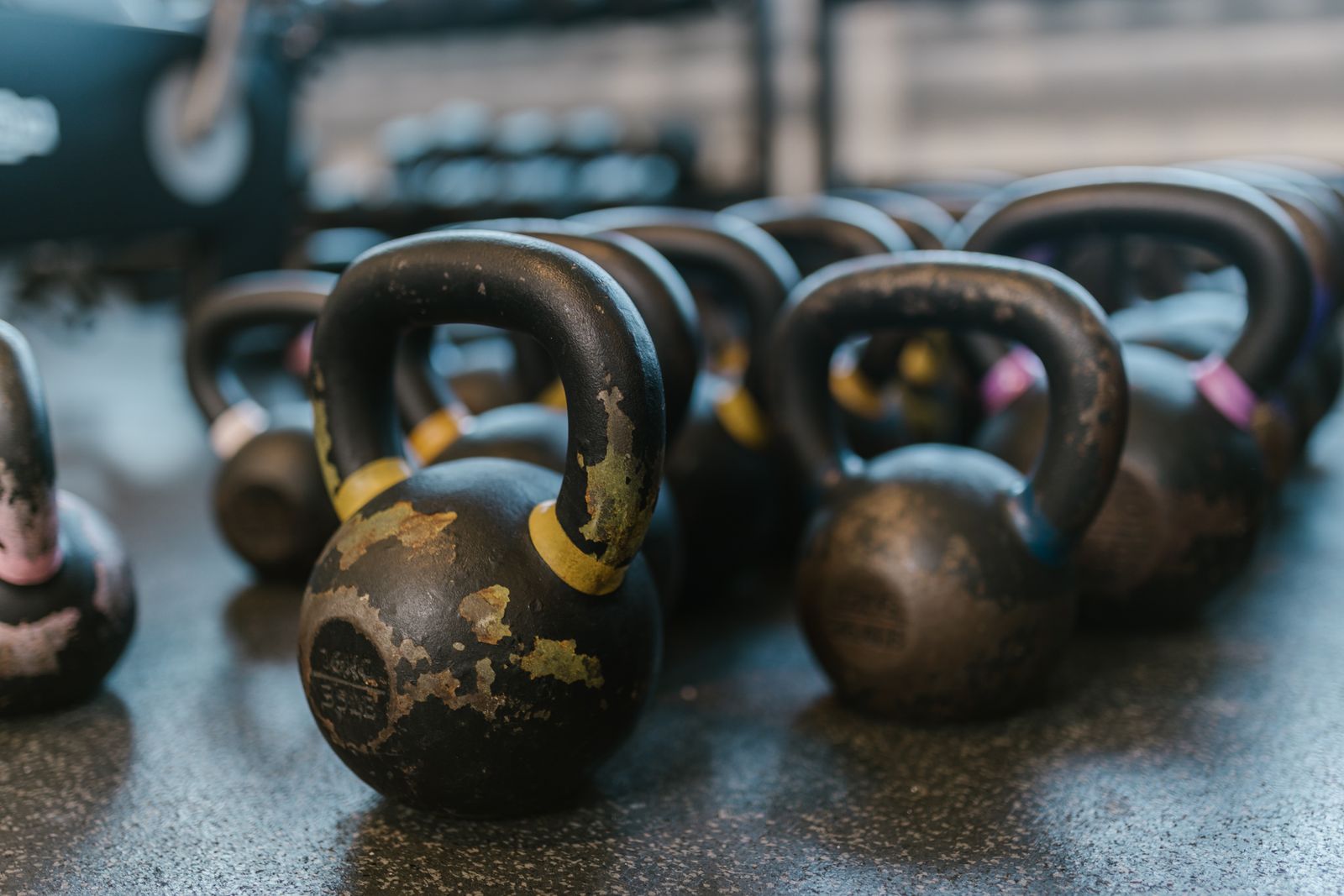 Rows of black cast-iron kettlebells with worn yellow paint resting on a speckled gym floor