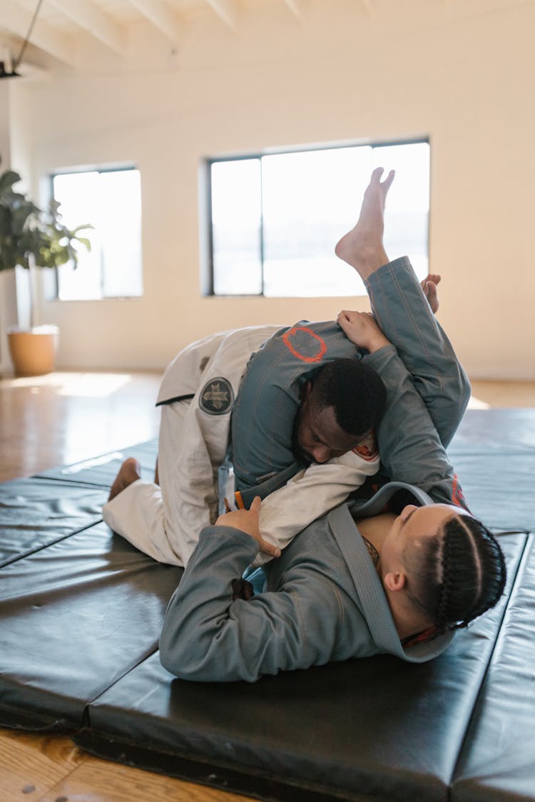 A Pair Of Men In Taekwondo Uniforms Sparring On Mat