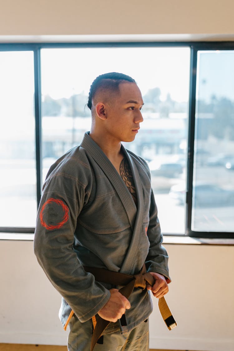 Man In Gray Kimono And Brown Belt Standing Beside Glass Window