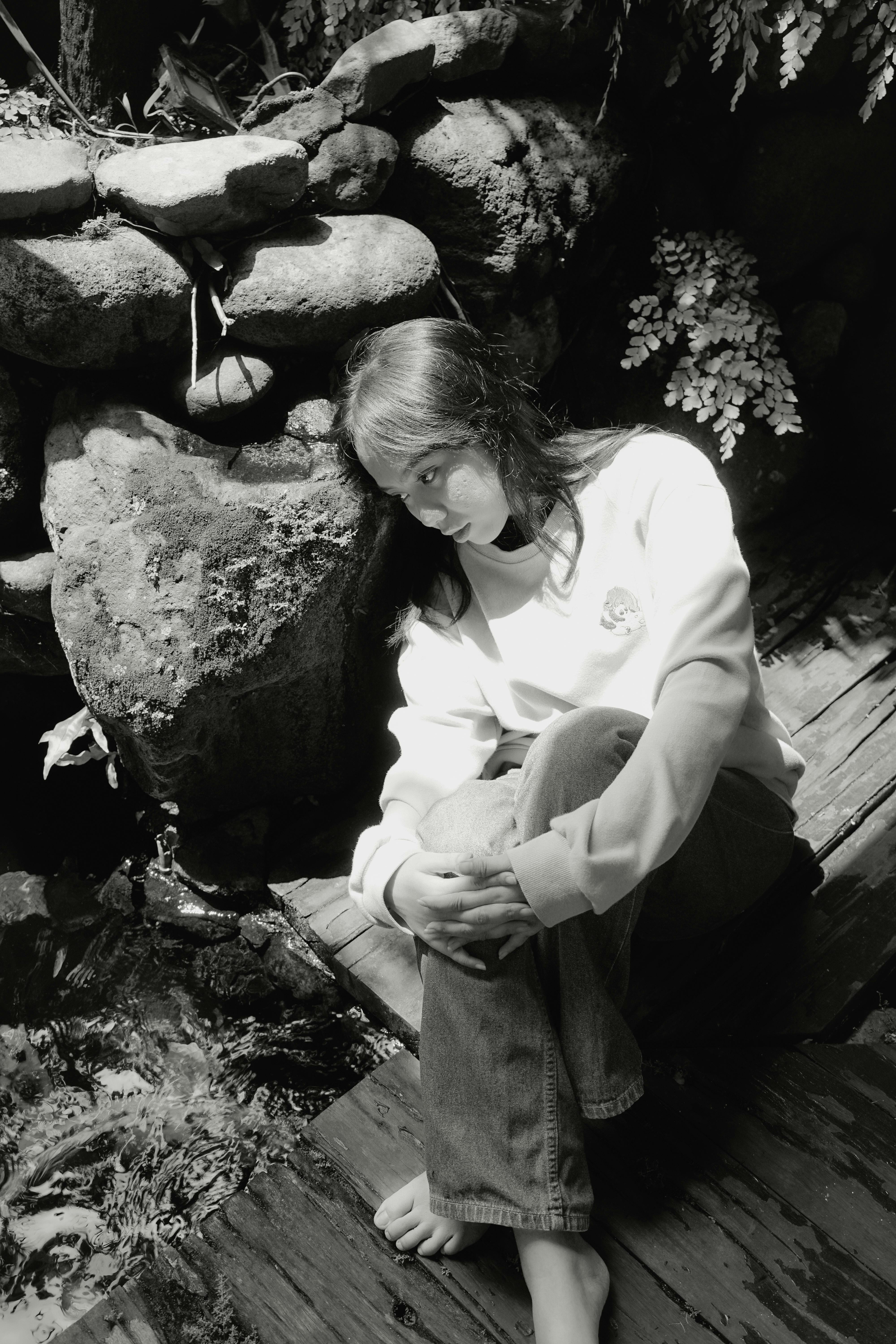 Monochrome portrait of a woman sitting on a wooden floor by a rock wall.