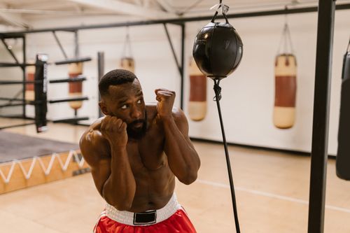 Free Shirtless boxer practicing with a punching bag in a boxing gym, focusing on fitness and strength. Stock Photo