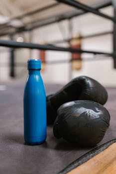 Close-up of a blue bottle and black boxing gloves on a gym ring floor