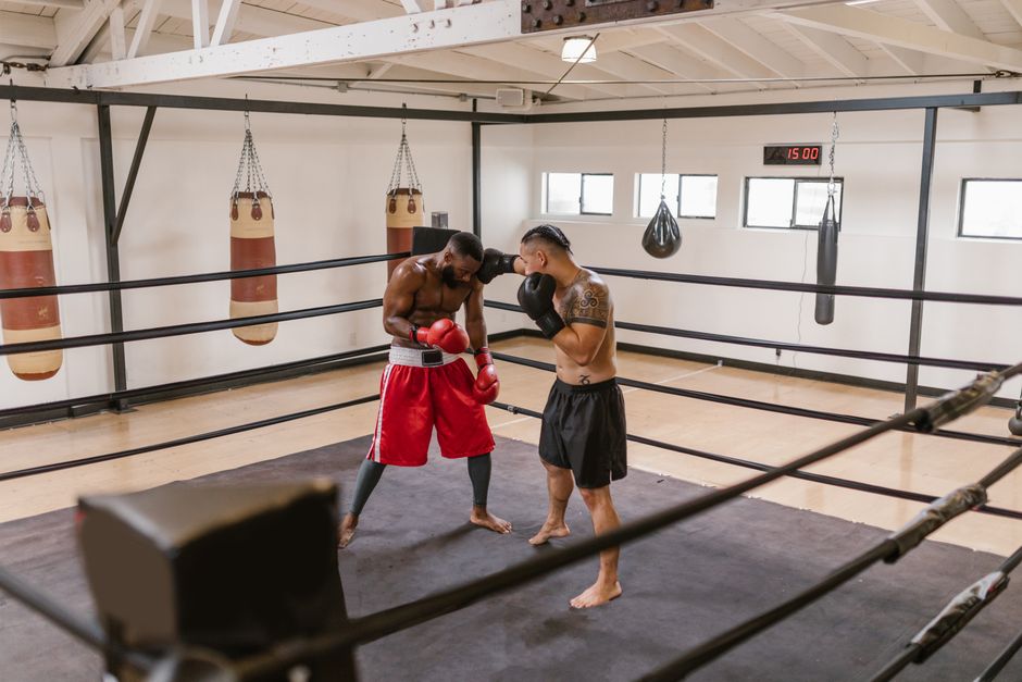 Two men engaged in a sparring session inside a boxing ring at an indoor gym with hanging punching bags. Two men engaged in a sparring session inside a boxing ring at an indoor gym with hanging punching bags.
