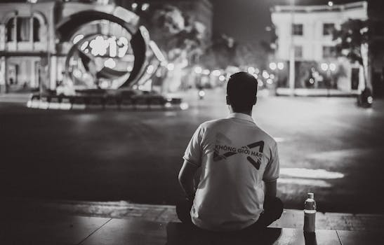 A man sits on city stairs at night, reflecting under city lights.