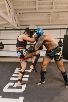 Two athletes sparring in a Muay Thai boxing ring indoors, showcasing powerful martial arts techniques.