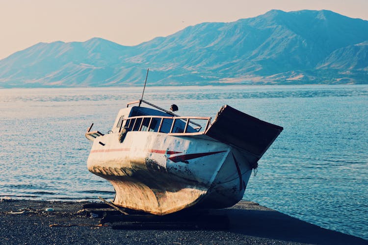 Old Boat On A Seashore And Mountains In Background