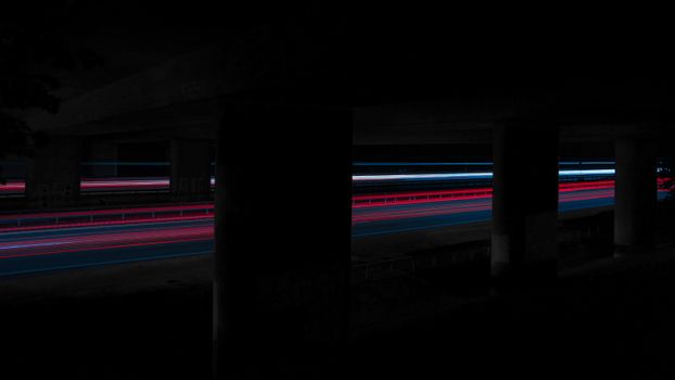 A stunning long exposure shot capturing vibrant light trails under a bridge at night.