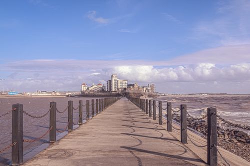 Free Long pier under a clear sky leading to seaside buildings, perfect for coastal exploration. Stock Photo