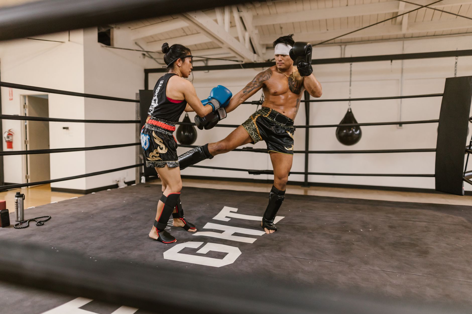 Two martial artists sparring in a gym boxing ring, showcasing fitness, skill, and martial arts.