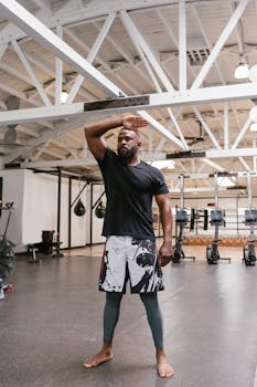 Man in athletic wear taking a break in a spacious, well-lit gym setting.