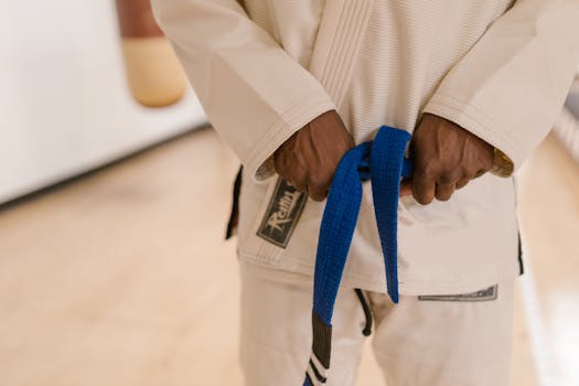 Close-up of a martial artist holding a blue belt, wearing a traditional uniform indoors.