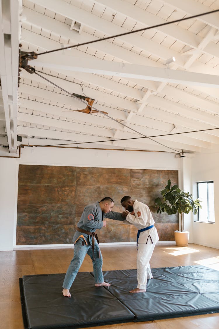 Two Men Wearing Karate Uniform Sparring On A Mat