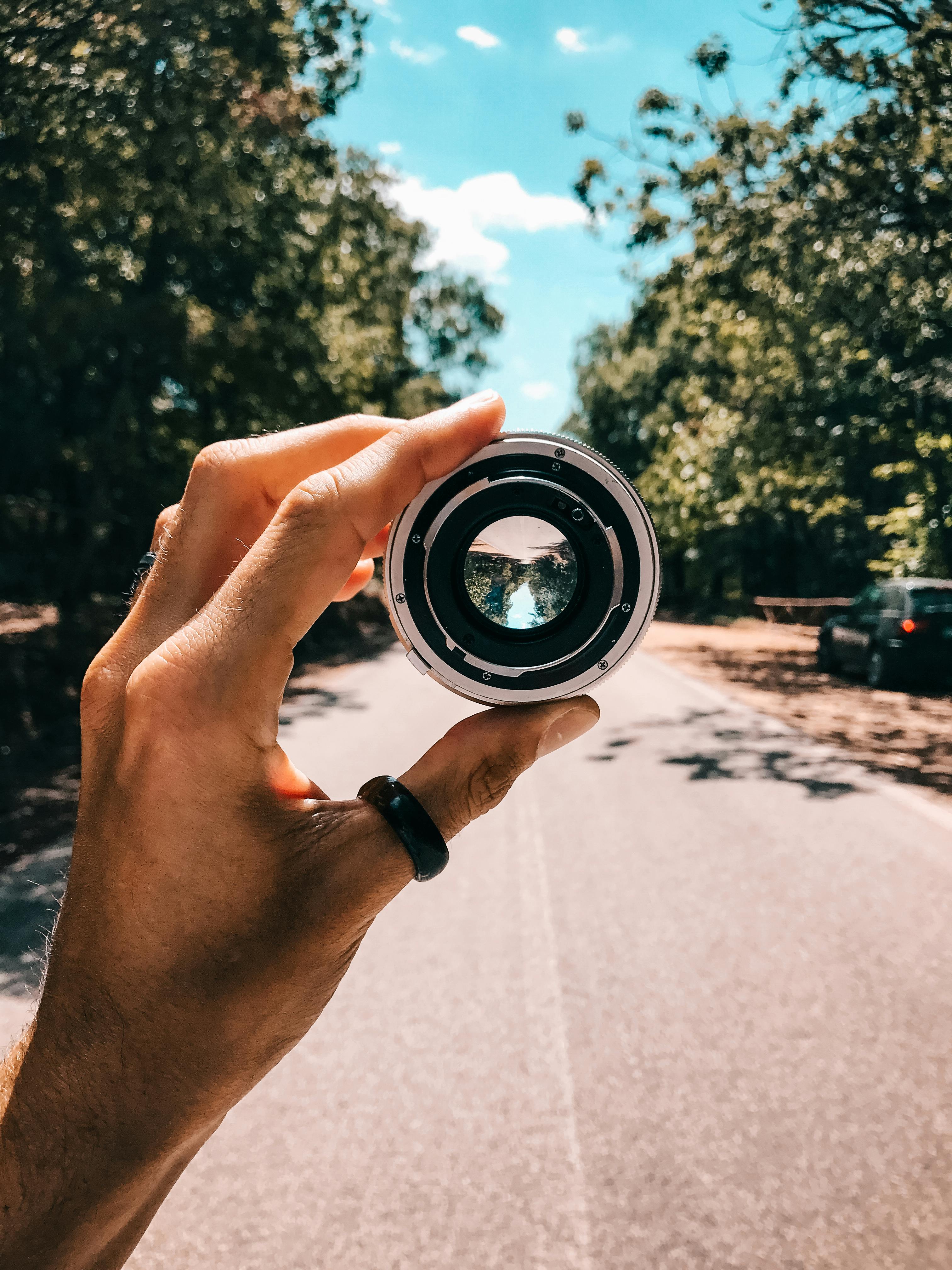 Person Holding Camera Lens In The Middle Of Street Under Blue Sky Free Stock Photo