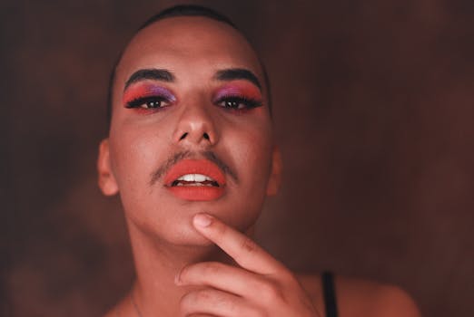 Close-up portrait of a person with vibrant eye makeup and orange lipstick, exuding confident expression.