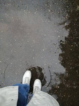 White sneakers standing in a puddle on a wet street in Obninsk, Russia, after a rain shower.